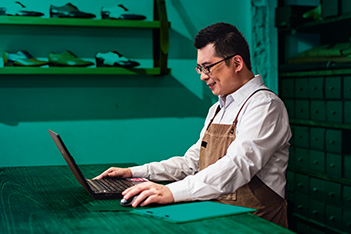 Safety professional man sitting in a shoe facility to look at his laptop and read about risk management