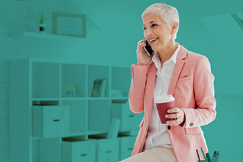 Safety professional woman with short white hair and a pink blazer is sitting on her desk and talking on the phone